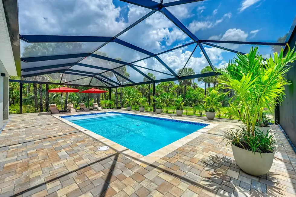Pool inside a screened lanai with a multicolour paver deck and potted palms