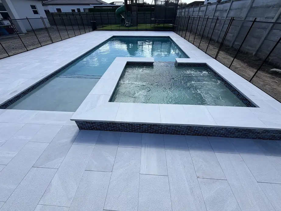 Rectangular pool with a raised spa in blue glass tile, a marble deck and a black child fence