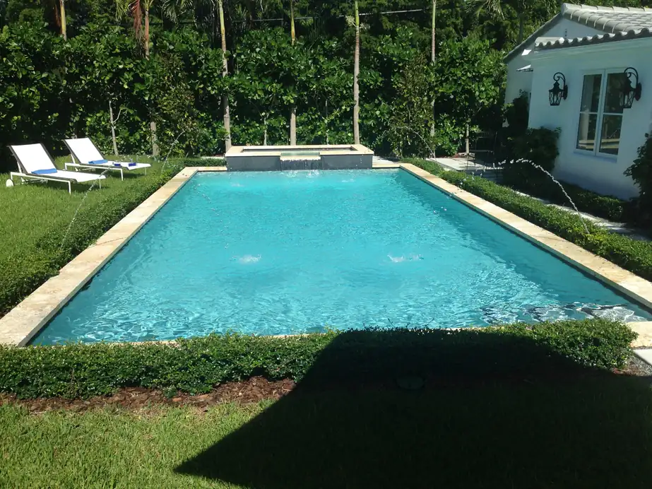 Bright aqua pool framed by clipped hedges and travertine coping