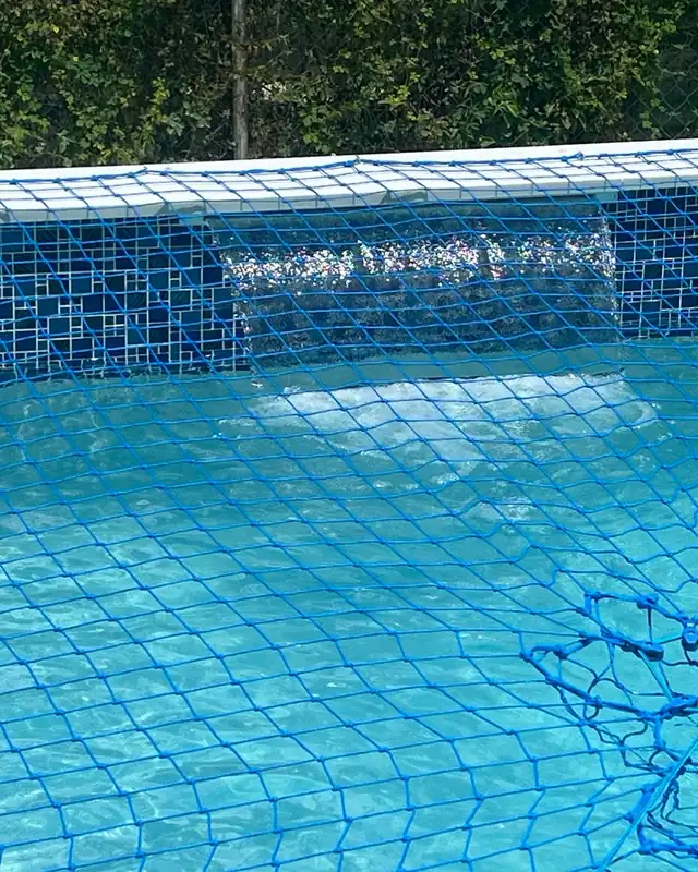 Blue safety net stretched over a pool with a tile spillway