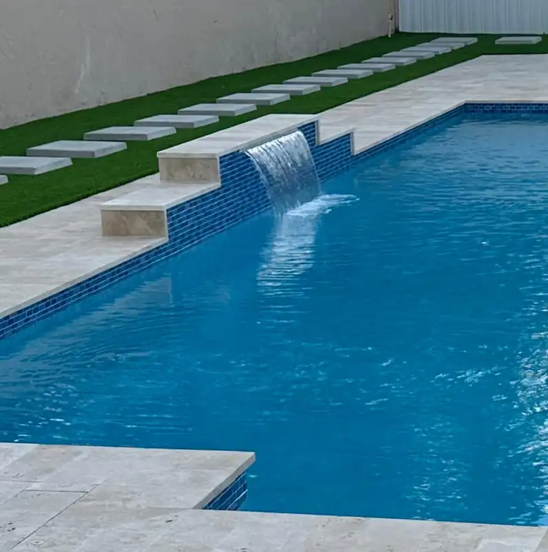 Spa spillway falling into a pool lined with blue glass tile, travertine coping and turf stepping stones