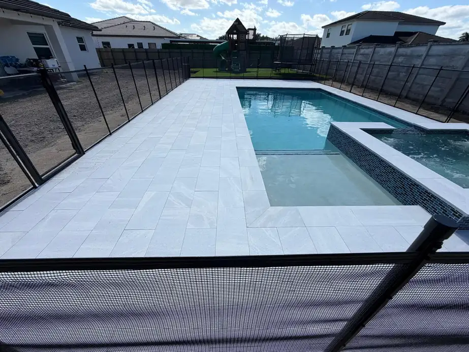 Marble pool deck around a pool with a raised spa and a black mesh safety fence