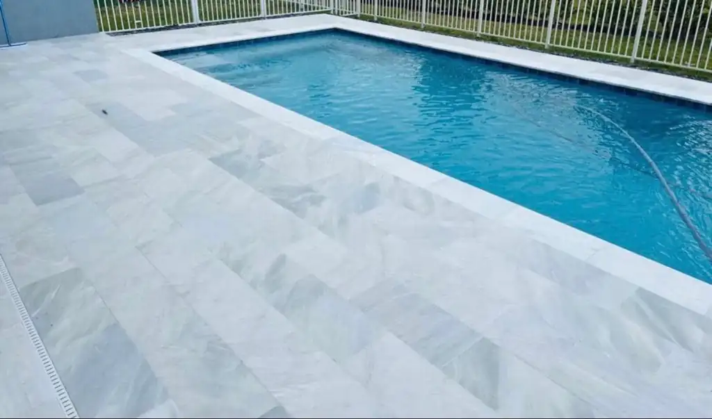 Rectangular pool with a wide pale marble deck and white picket fence