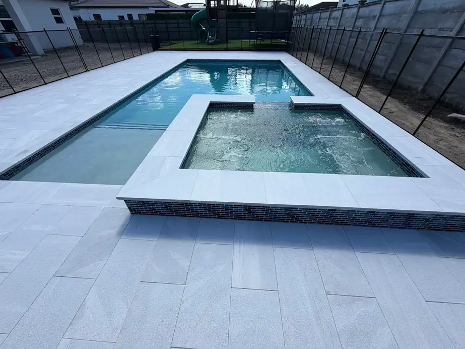 Pale marble deck and coping around a raised spa with mosaic tile set inside a pool