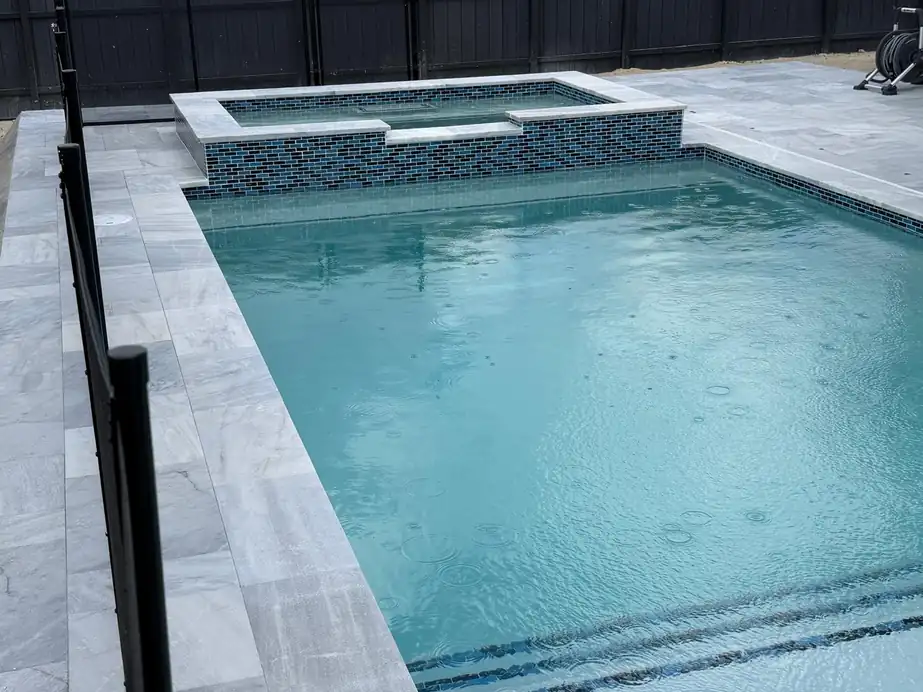 Raised spa with mosaic glass tile above pool steps, marble deck around it