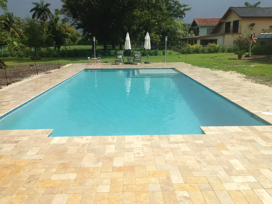 Long rectangular pool with a gold travertine deck and lawn beyond